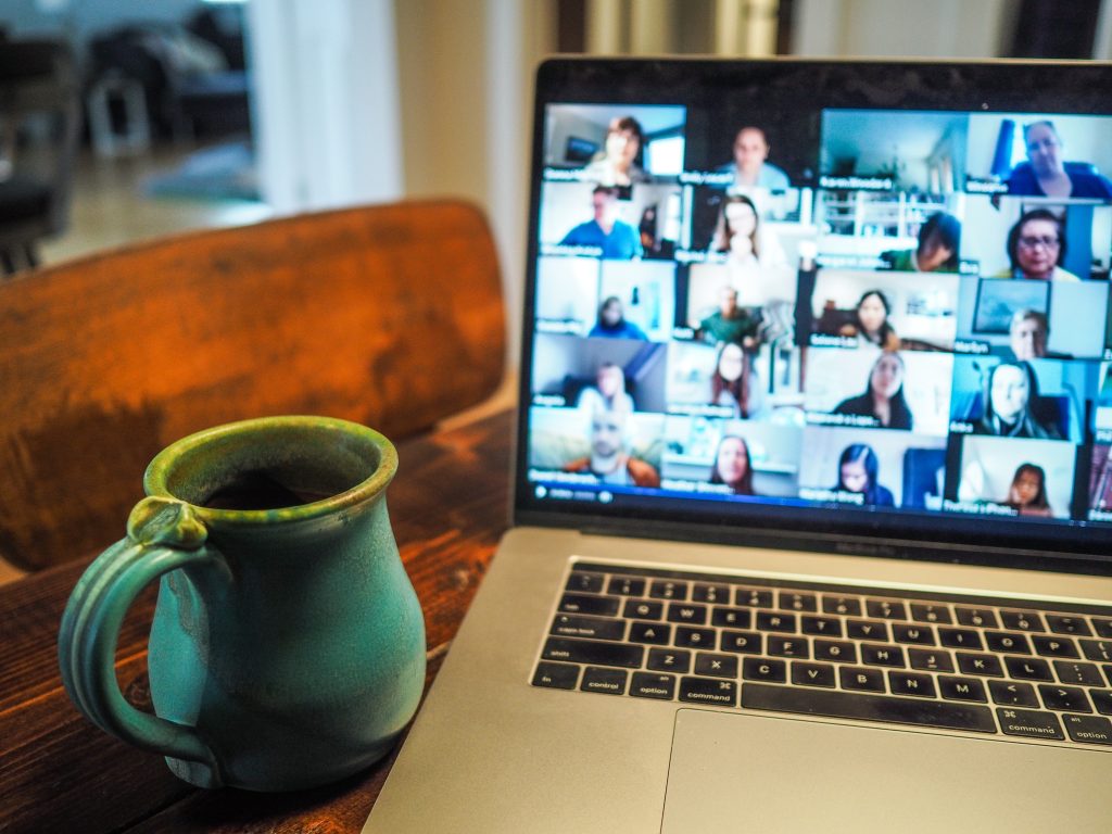 Laptop med bilde av mange deltakere i et nettmøte, og ved siden av en kaffekopp.