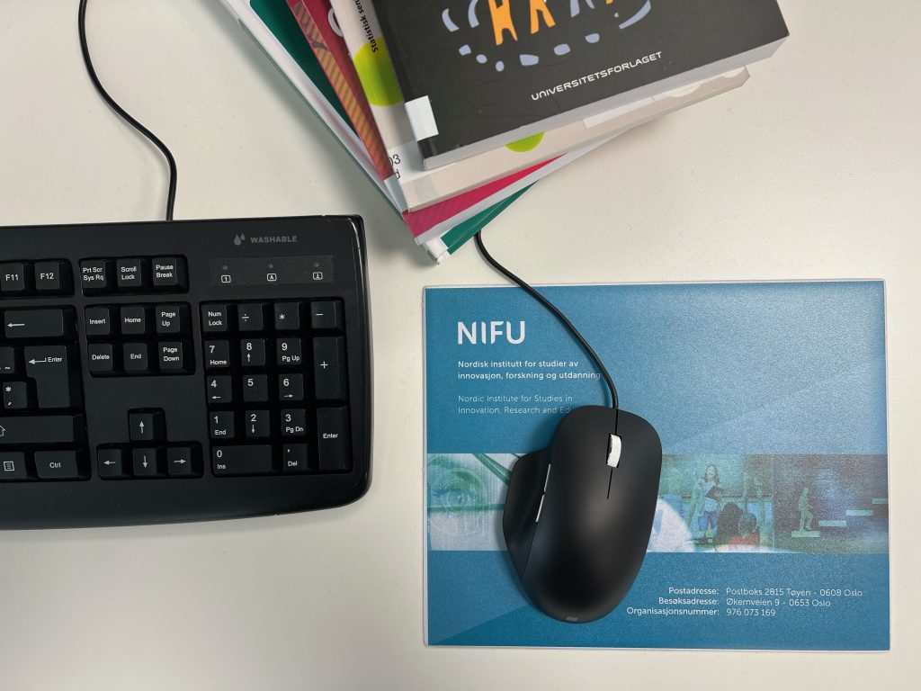 PC-tastatur med en mus og en bunke med bøker ved siden av.